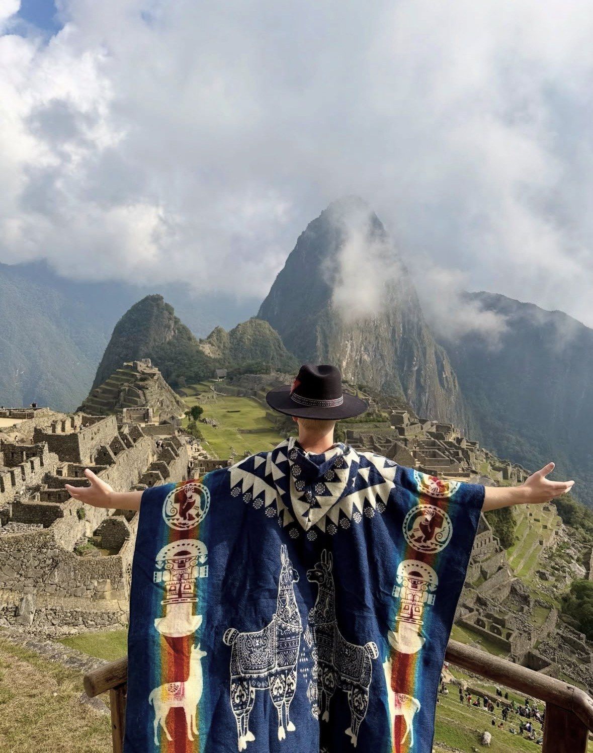 Traveller in patterned poncho and hat spreading arms above the ruins