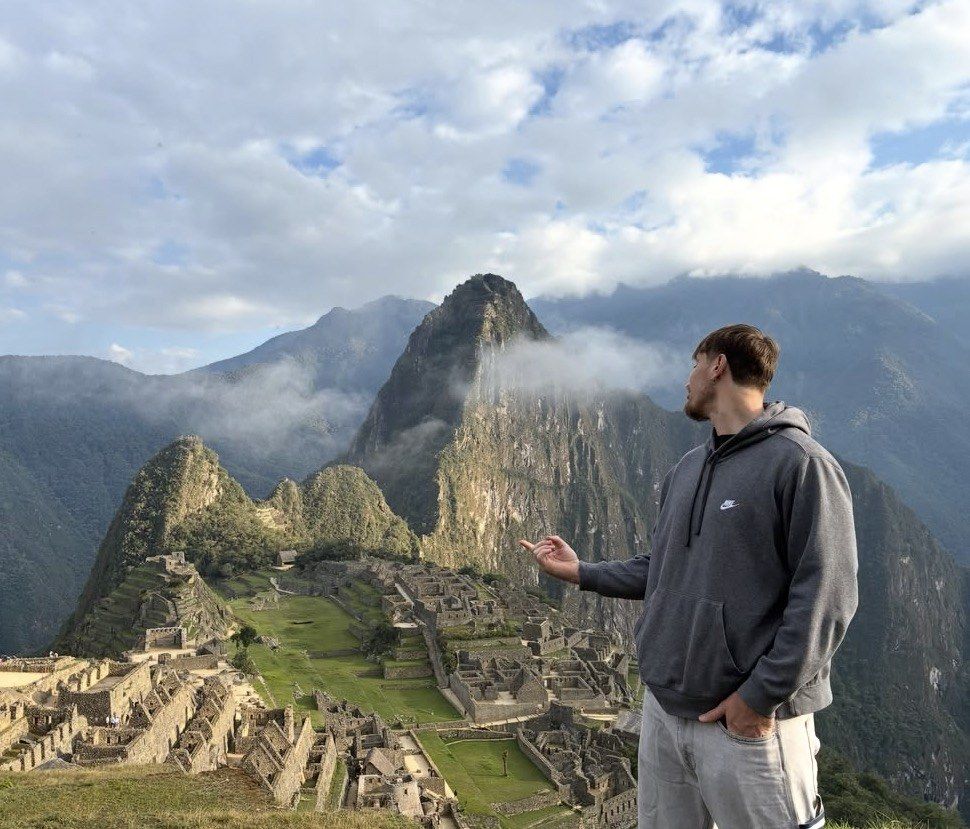 Man in grey hoodie gazing over Machu Picchu and cloudy valley