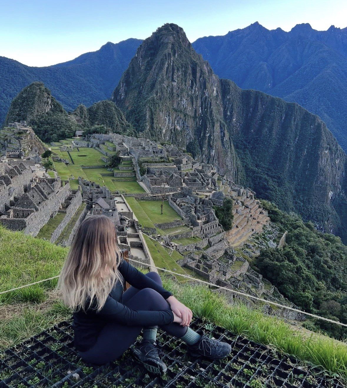 Woman sitting on the hillside terrace facing Machu Picchu at sunrise